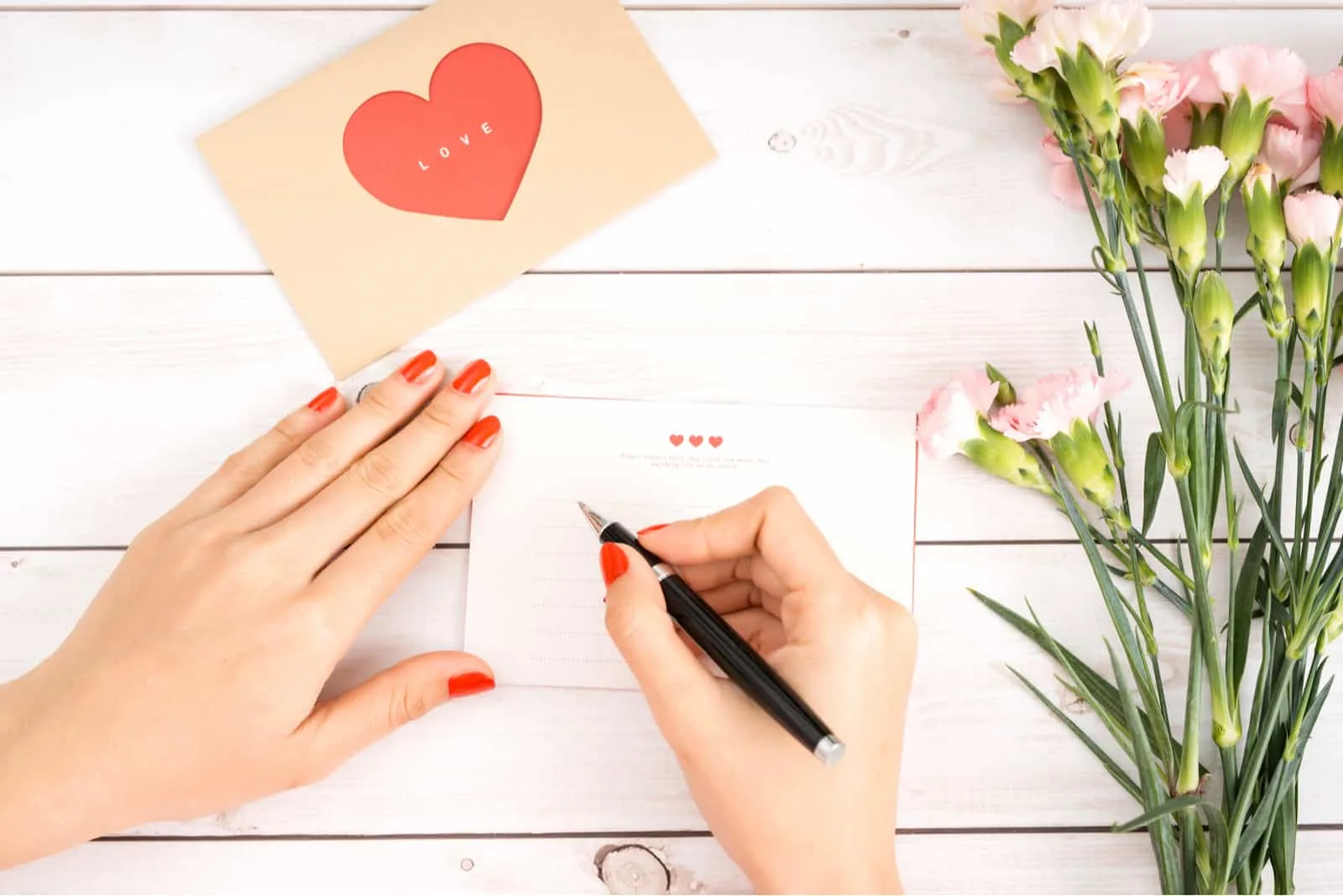 Frau schreibt Liebesbrief auf weißes Papier mit roter Herzform