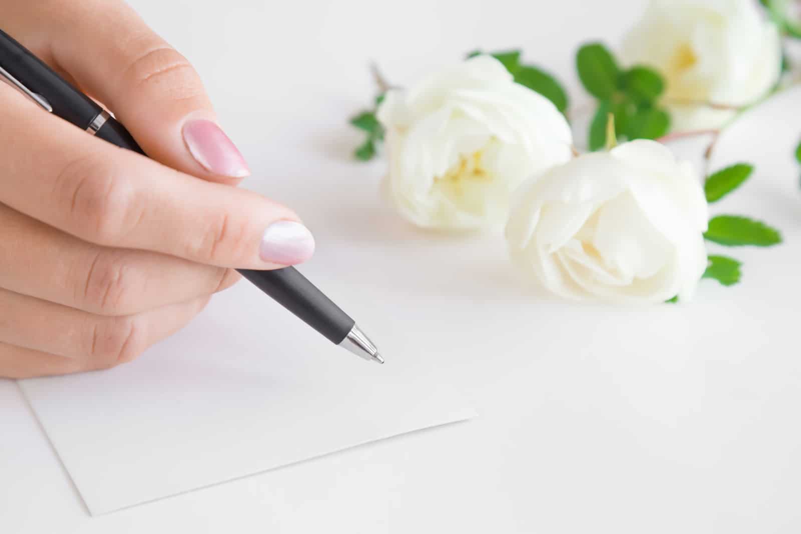 Frauenhand mit Stiftschrift auf der weißen leeren Grußkarte auf dem Tisch