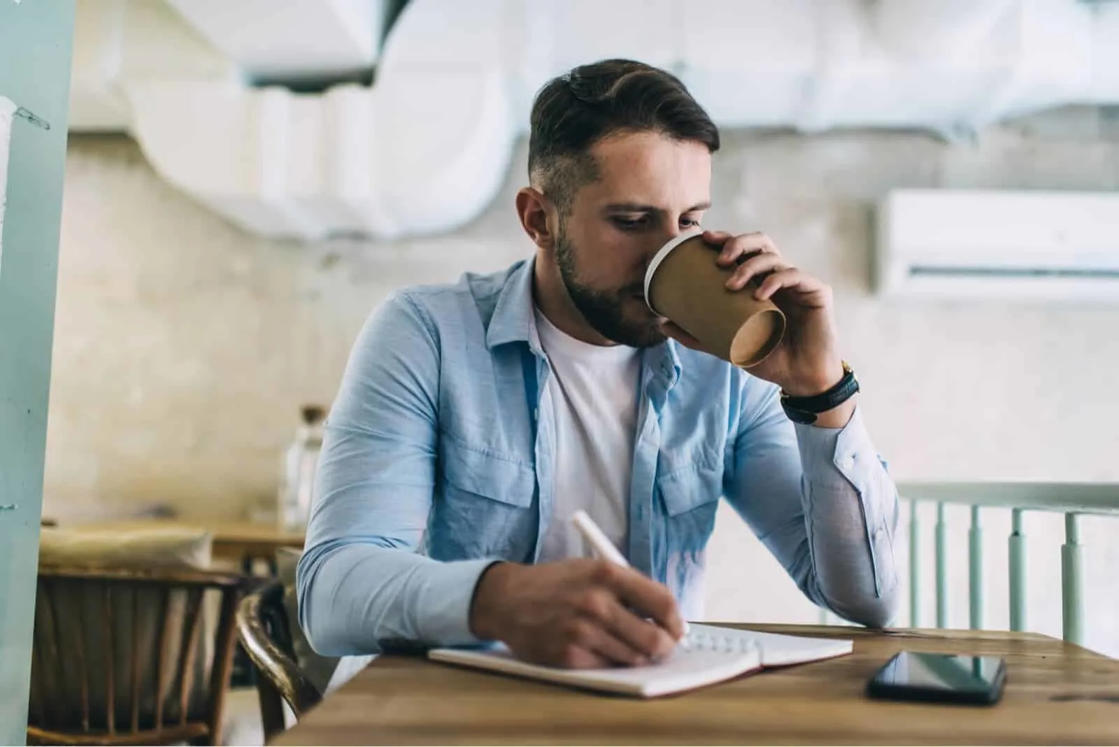 Ein Mann sitzt, trinkt Kaffee und schreibt