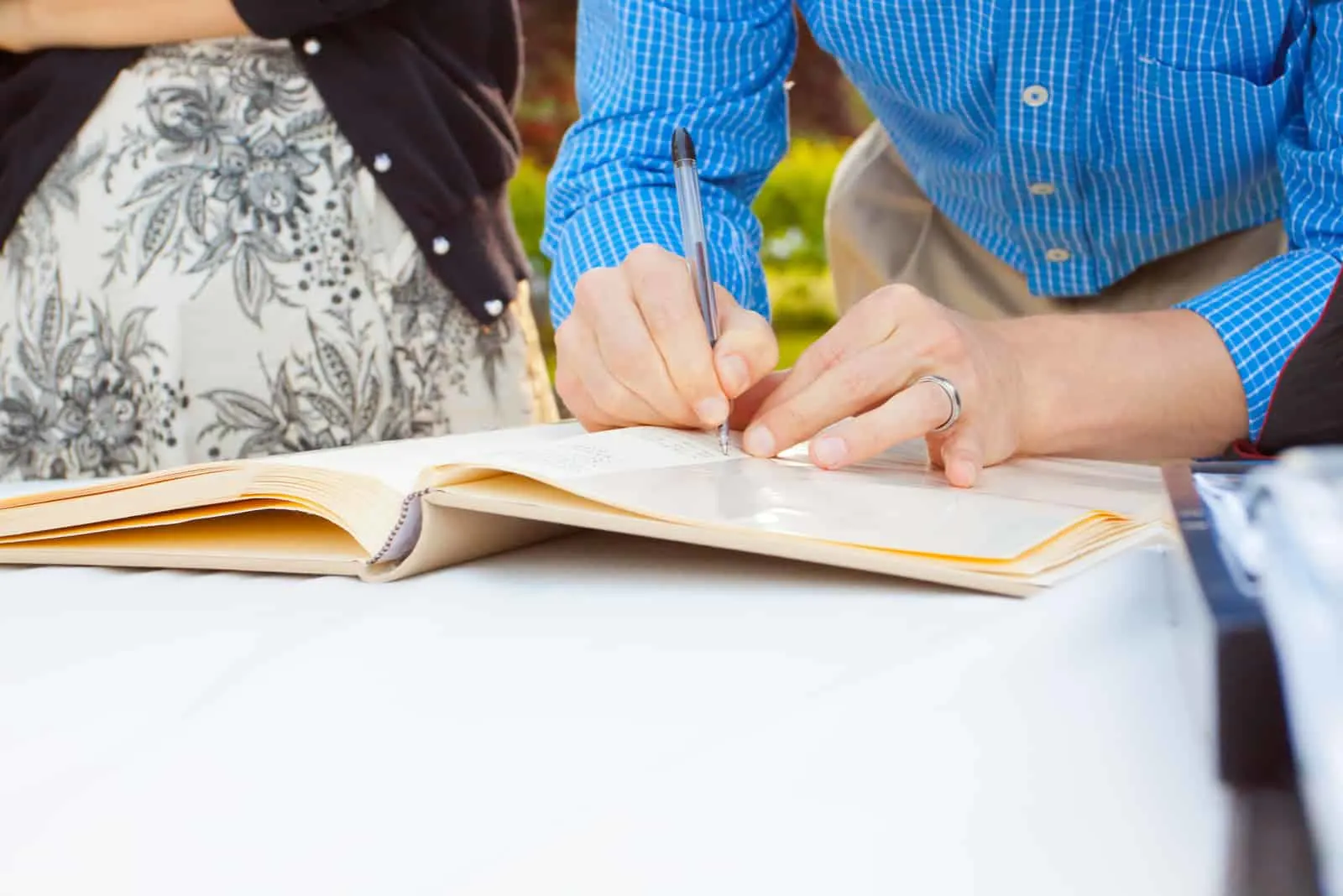 Ein Mann und eine Frau unterschreiben ein Hochzeitsgästebuch mit einem Stift.