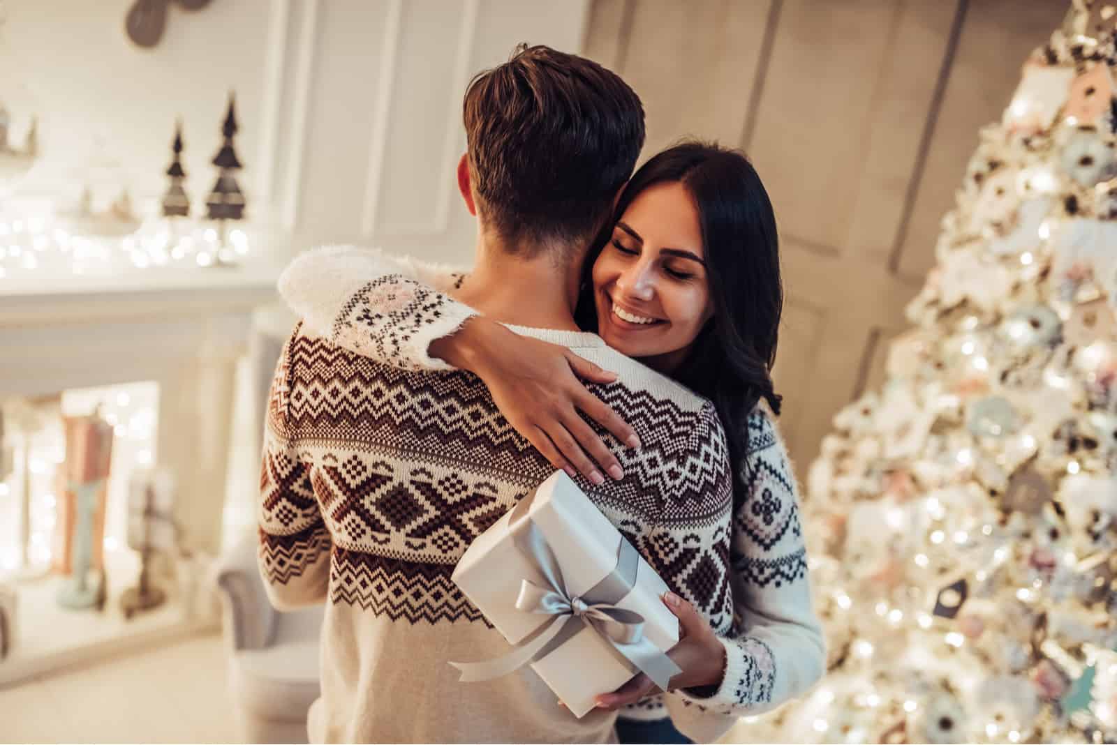 Frau, die Mann umarmt und Geschenkbox in der Hand hält