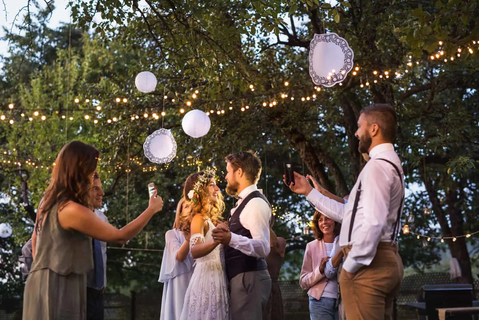 Gäste mit Smartphones fotografieren Braut und Bräutigam auf der Hochzeitsfeier draußen