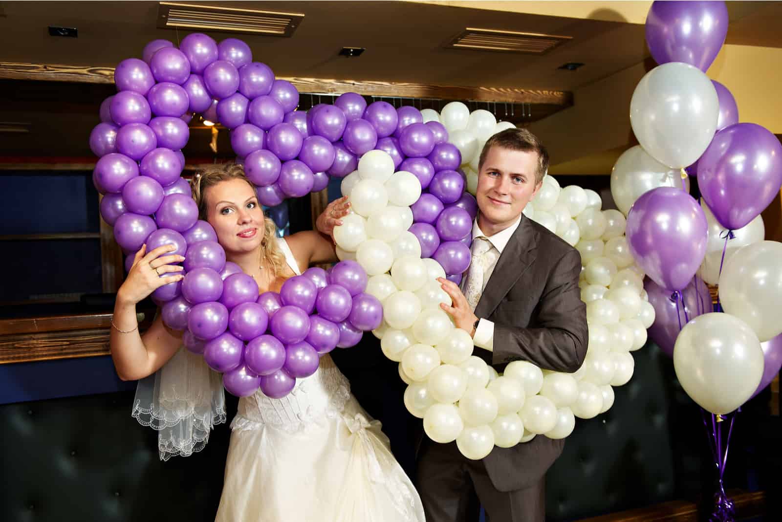 Glückliches Brautpaar mit lila und weißen Luftballons