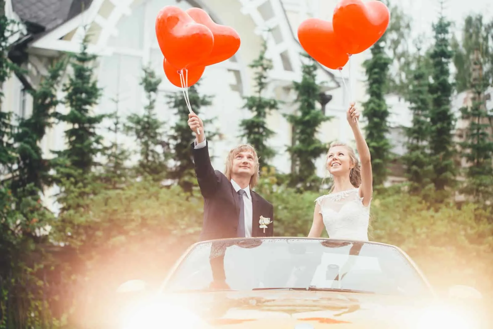 Hochzeitspaar im Auto mit Luftballons in den Händen