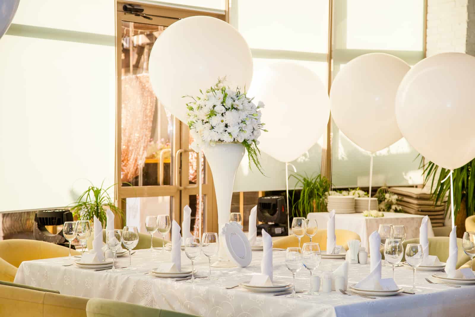 Hochzeitstische im Restaurant mit weißen Blumen und riesigen weißen Luftballons