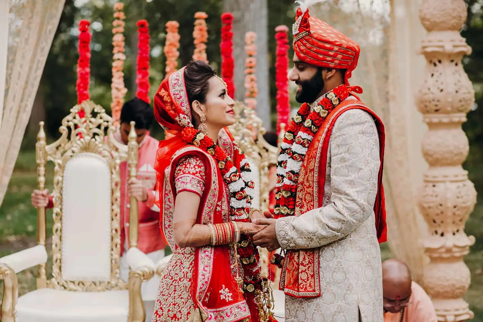 Indischer Bräutigam gekleidet in weißem Sherwani und rotem Hut mit atemberaubender Braut