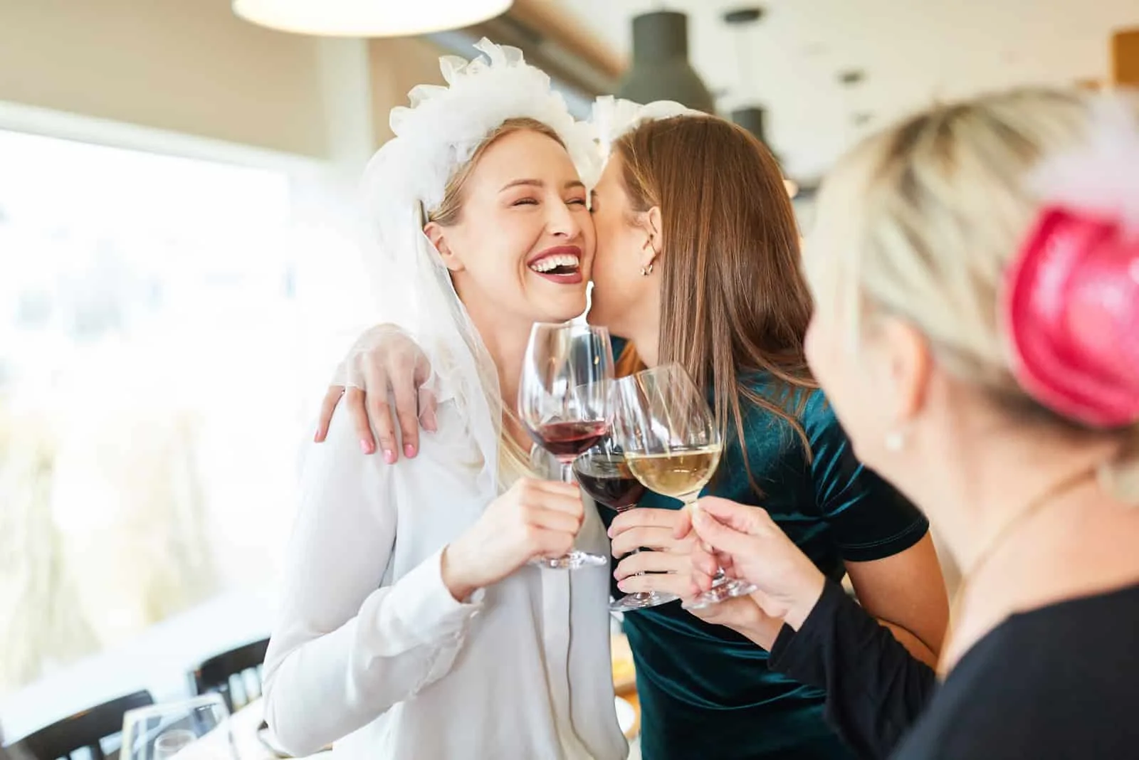 Lachende Braut mit Brautschleier wird von Freundin im Restaurant umarmt