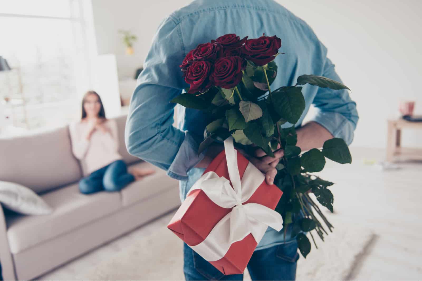 Männerhände verstecken sich mit schickem Strauß roter Rosen und Geschenk