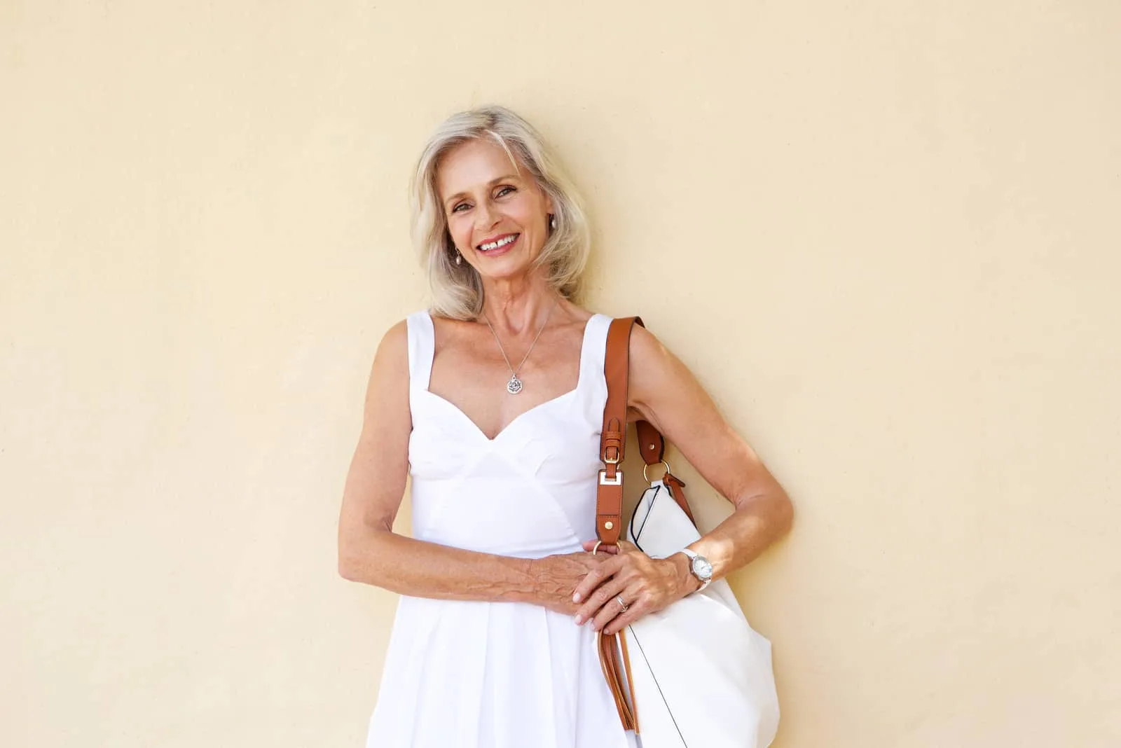 Porträt der glücklichen älteren Frau, die im weißen Kleid mit Geldbörse steht