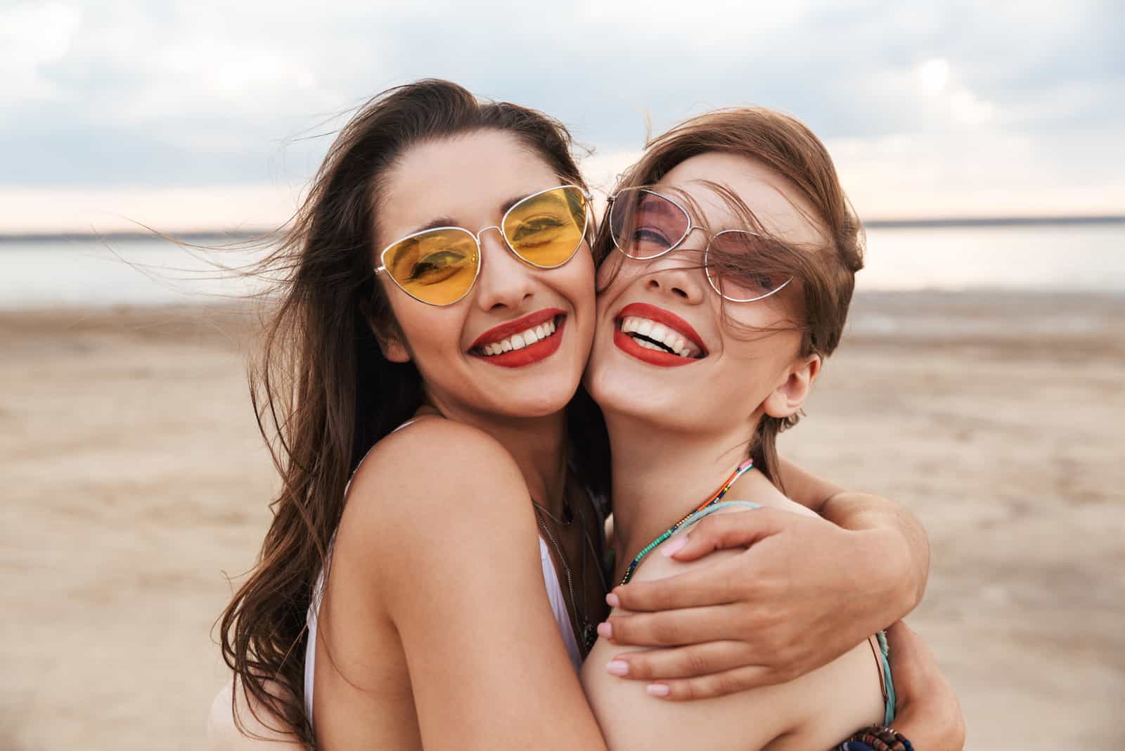 Zwei fröhliche junge Freundinnen verbringen eine gute Zeit am Strand und lachen