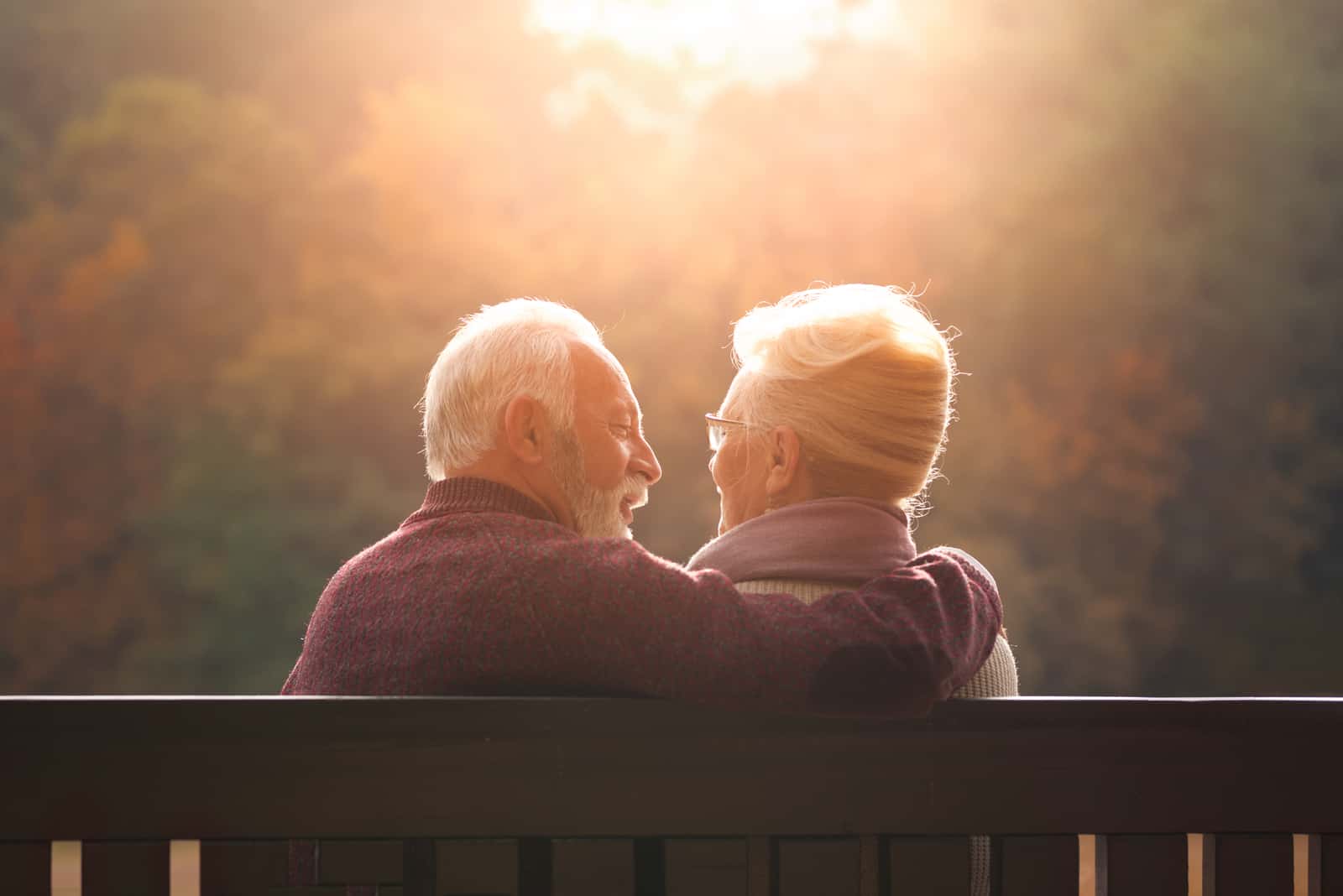 Älteres Paar, das auf Bank im Herbstpark sitzt und Sonnenuntergang schaut