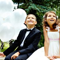 Porträt der Kinderbraut und des Bräutigams mit Luftballons, die im Park sitzen