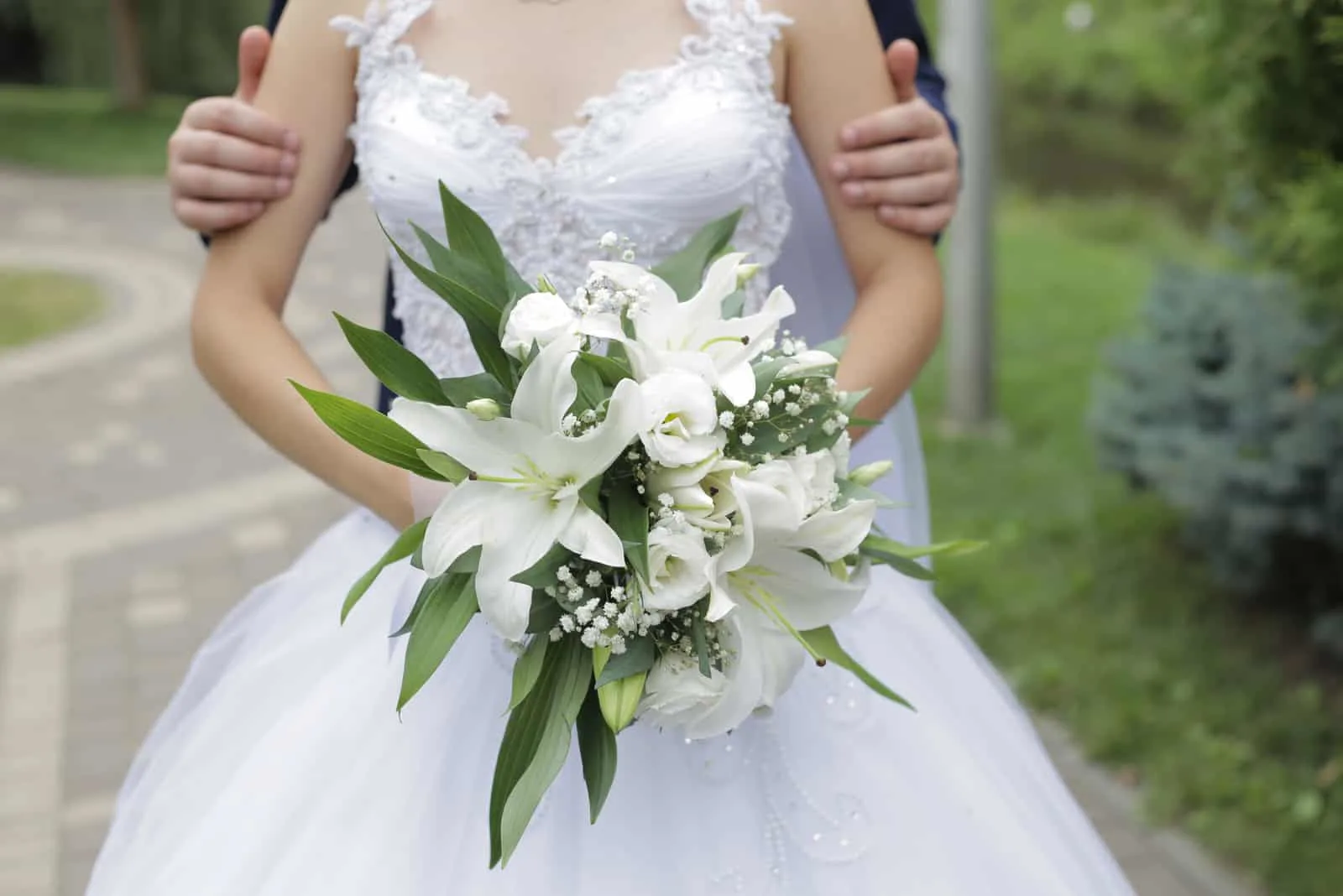 Braut und Bräutigam werden im Park mit einem Strauß weißer Lilien fotografiert