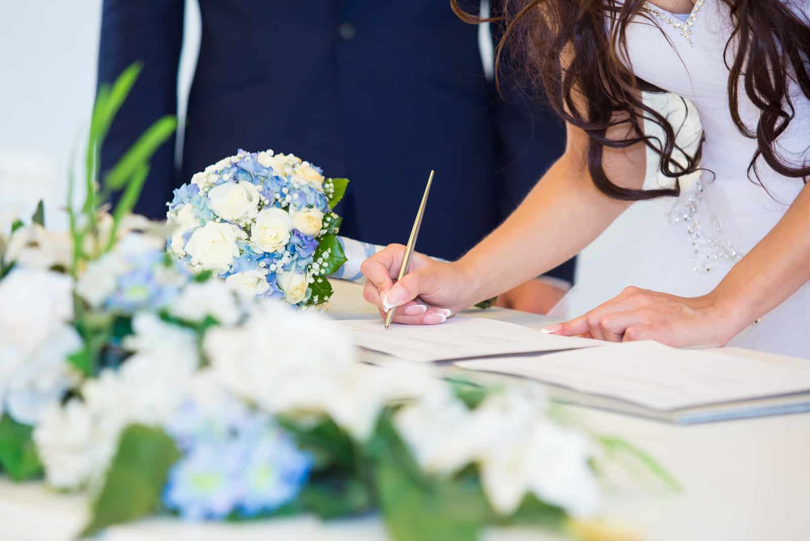 Brauthand mit einem Stift, der Hochzeitslizenz unterzeichnet