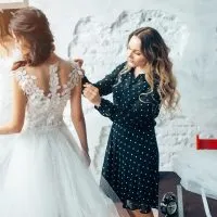 Die Frau hilft, das Hochzeitskleid der Braut anzuziehen