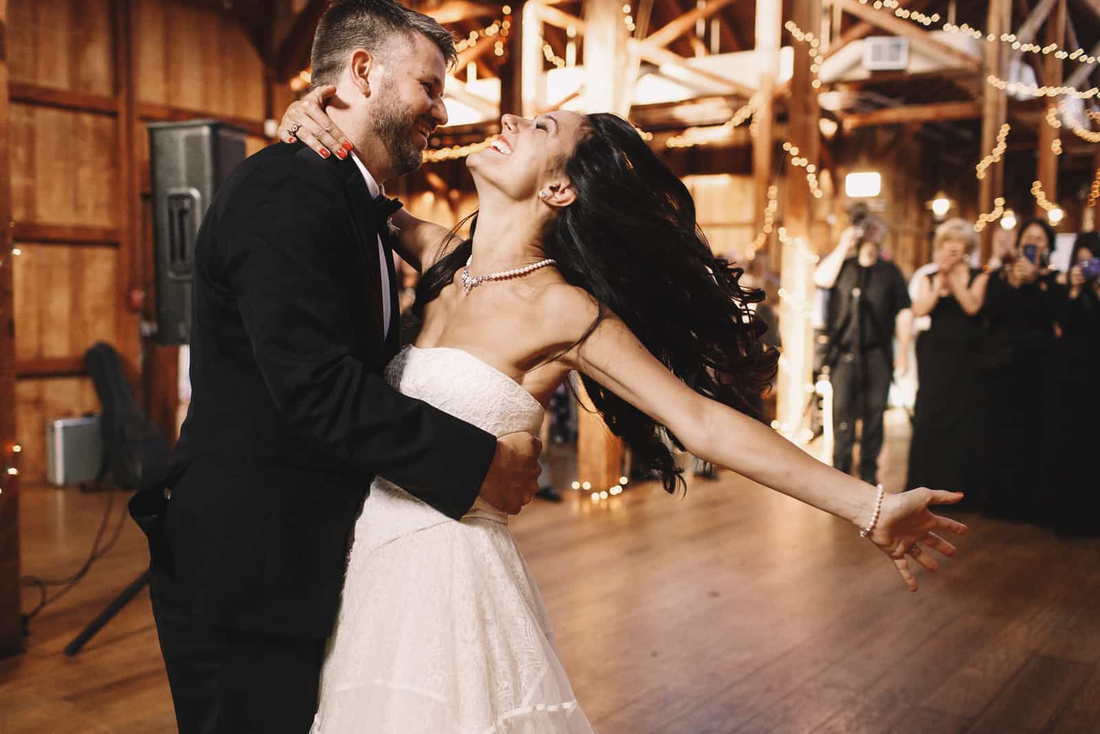 Die Braut schüttelt ihr dunkles Haar, während sie mit einem Bräutigam in einer Holzhalle tanzt