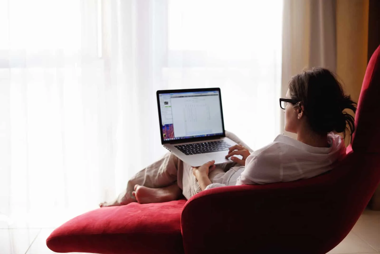 Eine Frau mit Brille sitzt in einem Sessel und benutzt einen Laptop