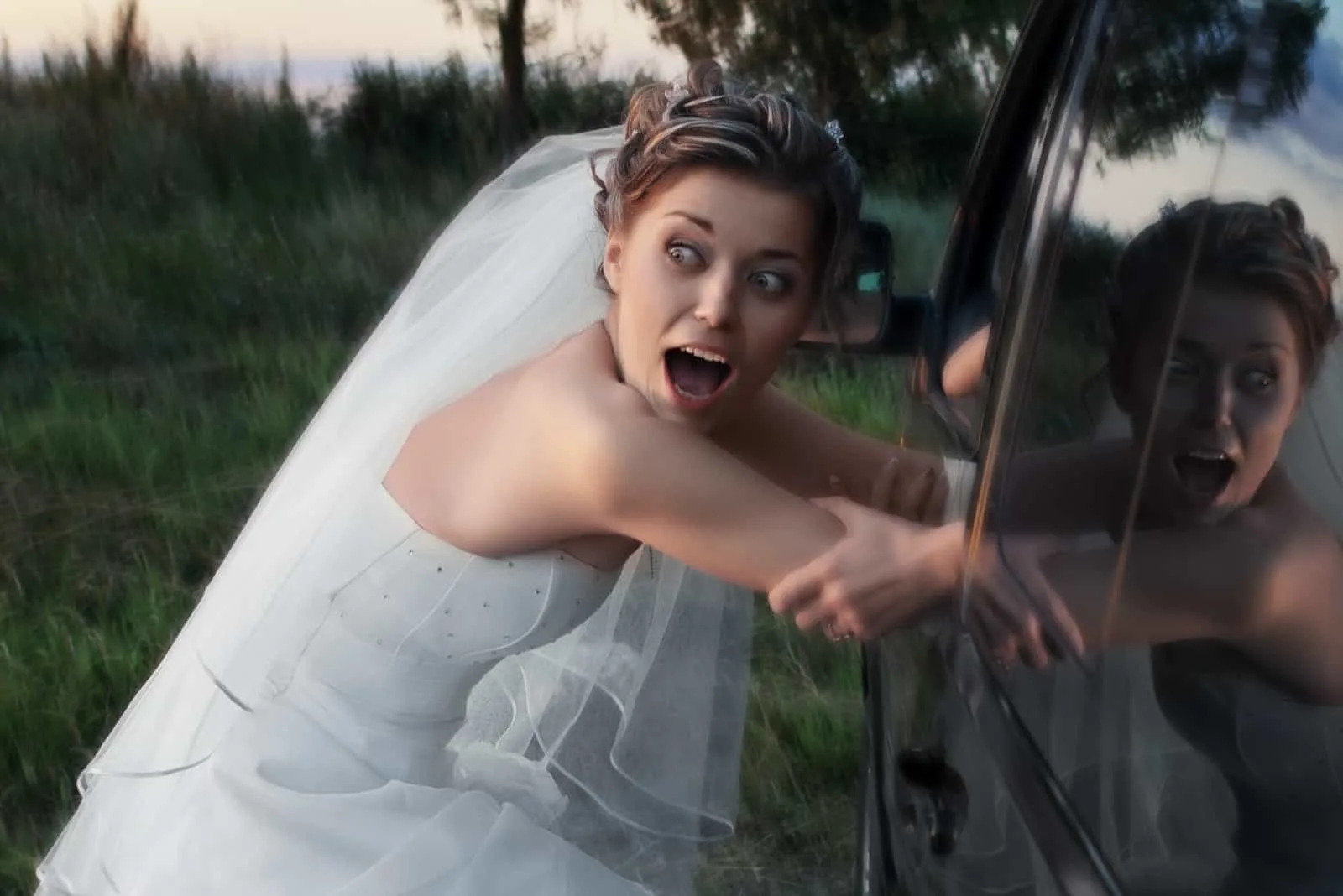Erschrockene Braut im weißen Kleid, die abends in ein schwarzes Auto entführt wird