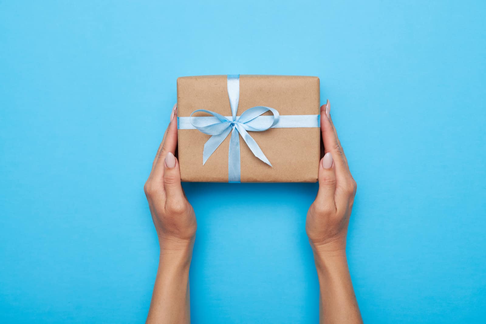 Frauenhände halten Geschenk verpackt und verziert mit Bogen auf blauem Hintergrund