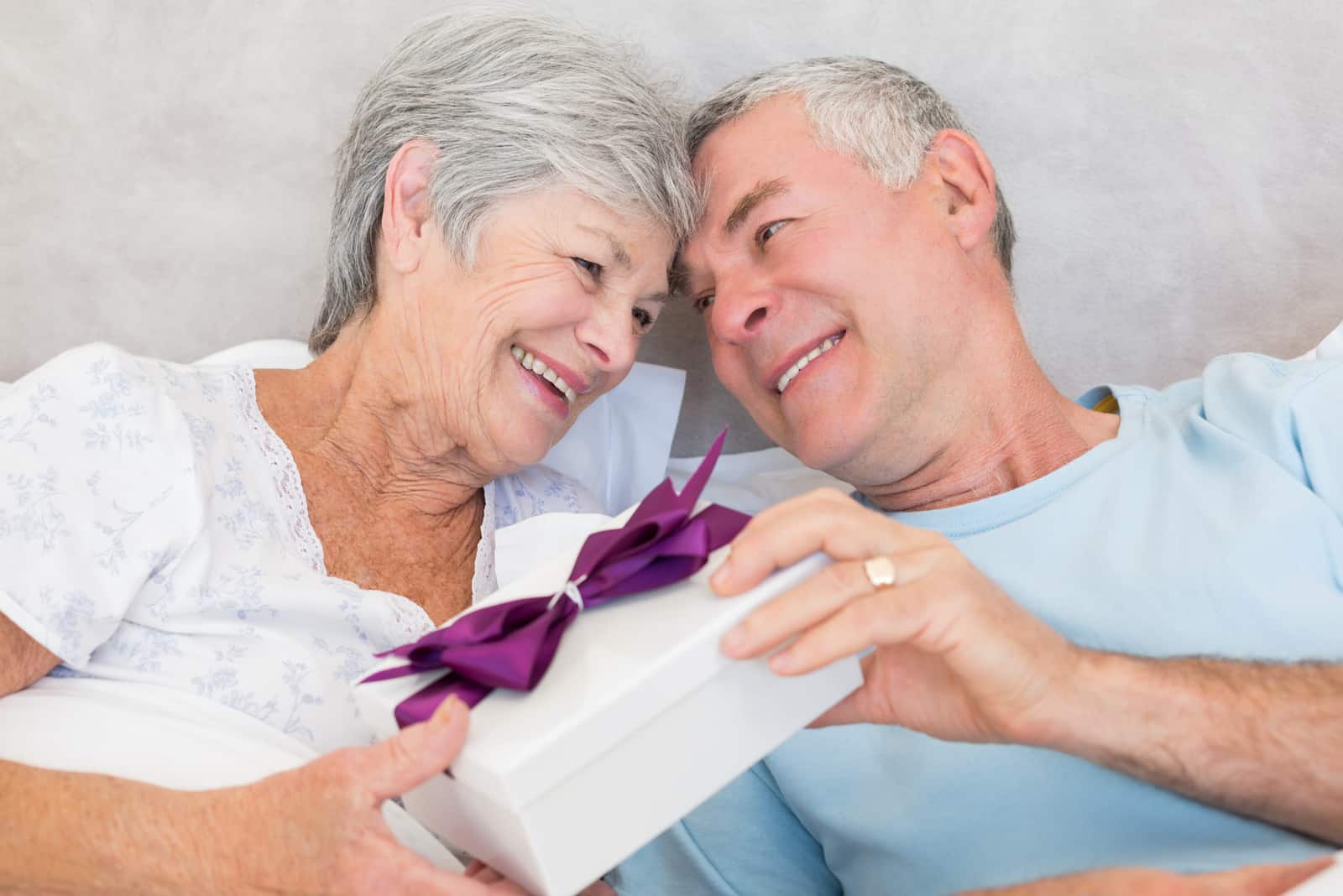 Glückliches älteres Paar, das Geschenkbox austauscht, während zu Hause im Bett entspannt