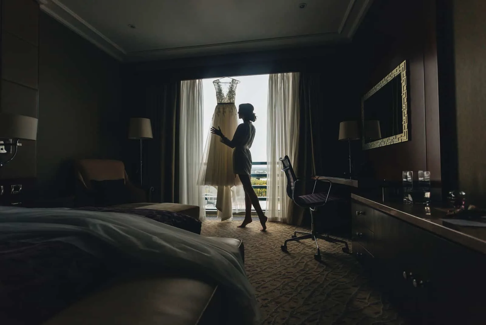 Im Raum am Fenster steht eine Frau, die ein Hochzeitskleid betrachtet