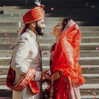 Indischer Bräutigam gekleidet in weißem Sherwani und rotem Hut mit atemberaubender Braut