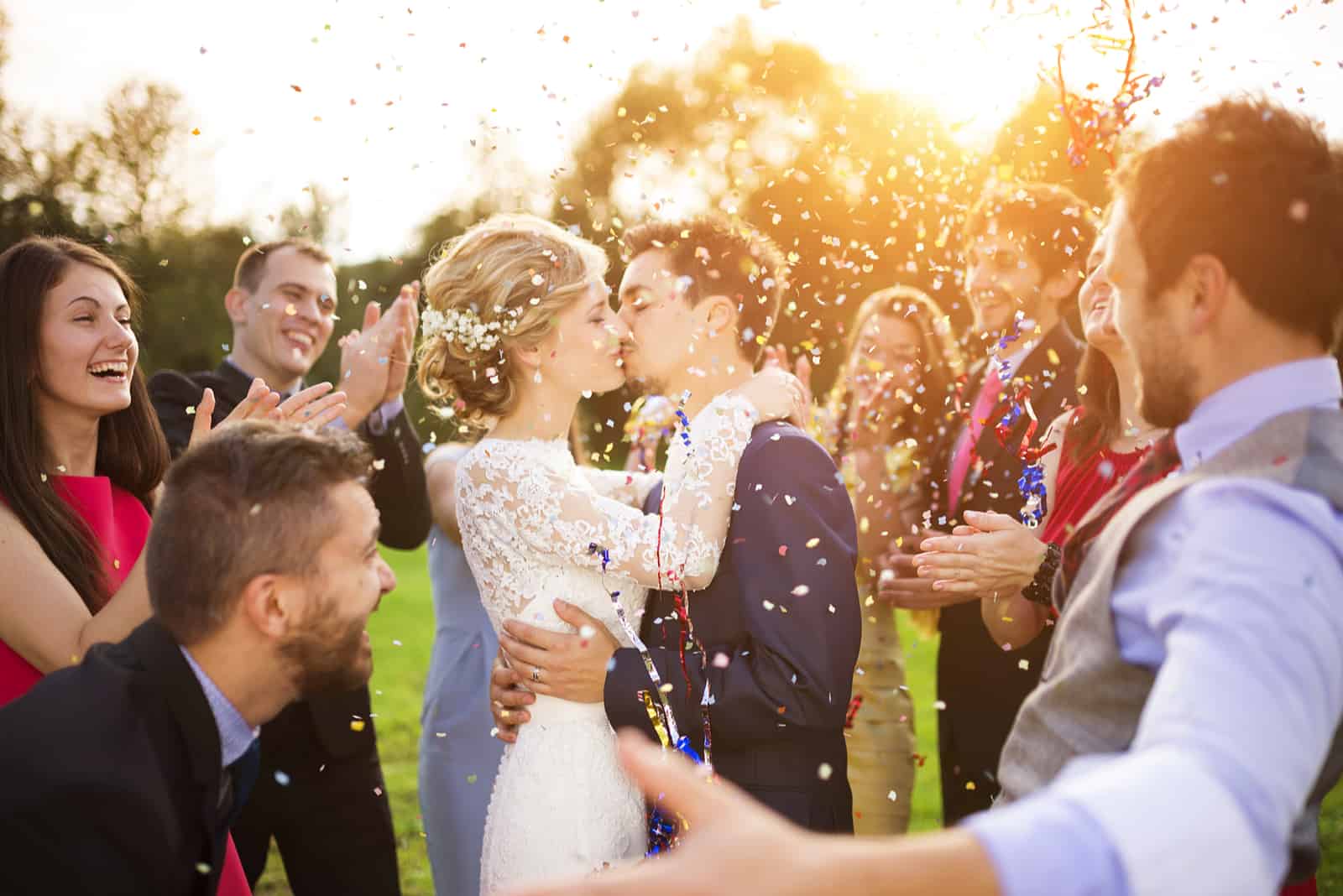 Jungvermähltenpaar und ihre Freunde auf der Hochzeitsfeier duschten mit Konfetti im grünen, sonnigen Park