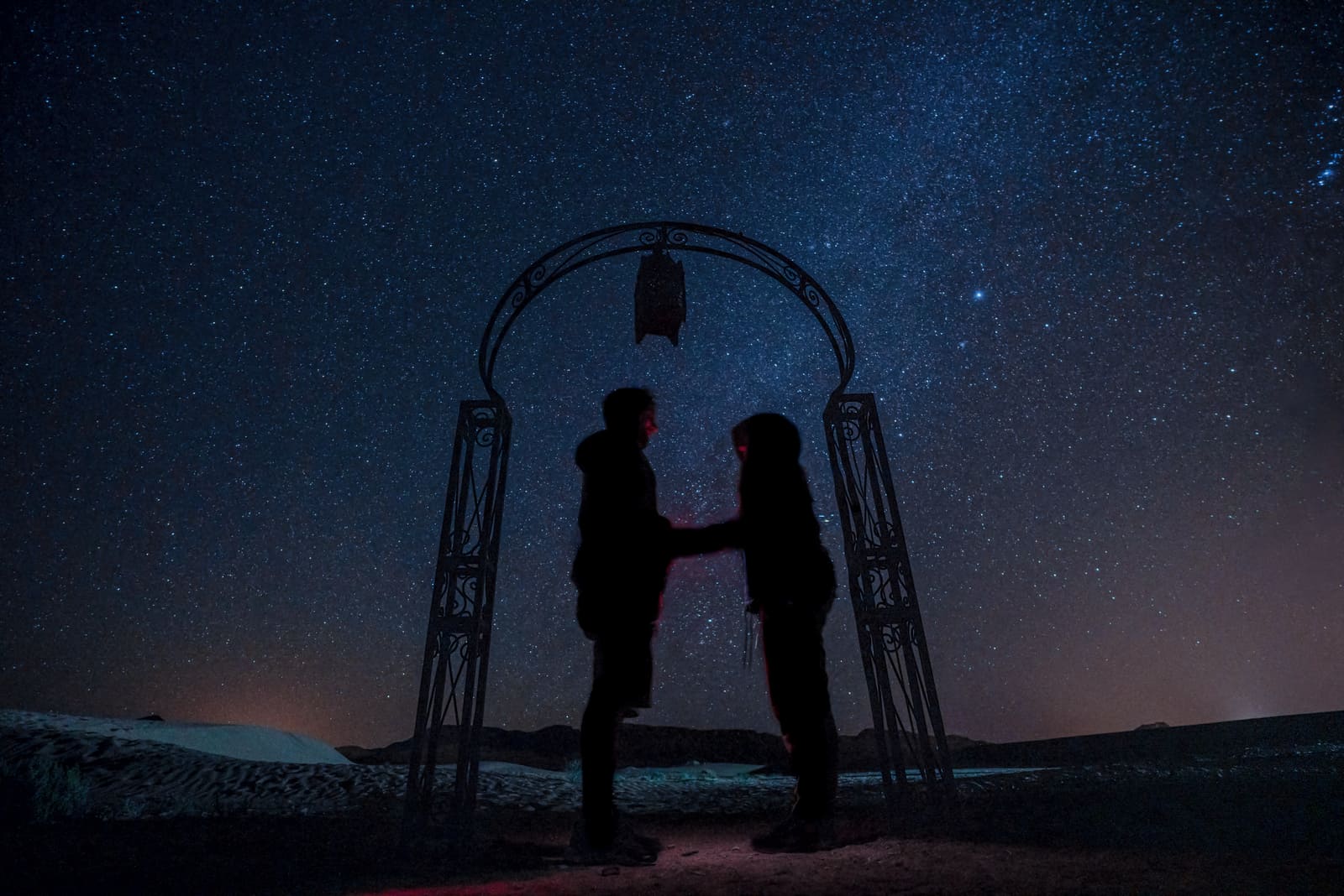 Nachtsilhouette eines verliebten Paares Händchen haltend in der Wüste unter den Sternen