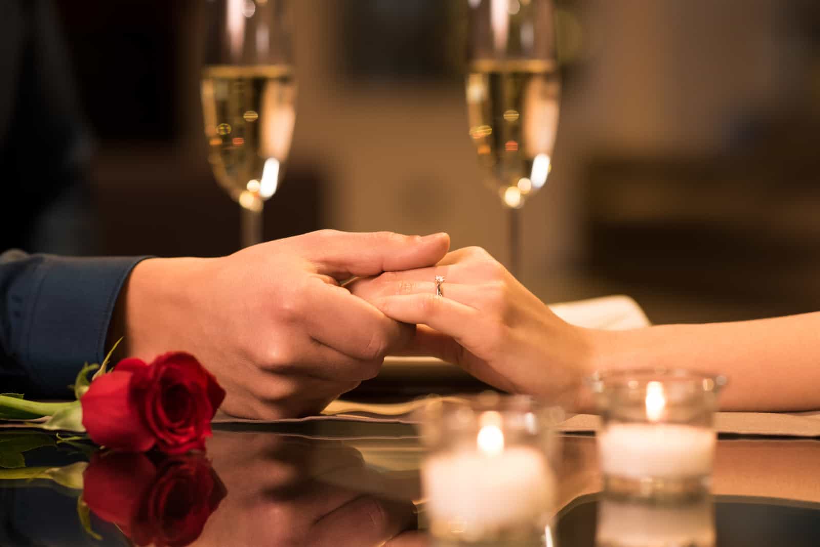 Paar Hände auf Restauranttisch mit zwei Gläsern Champagner
