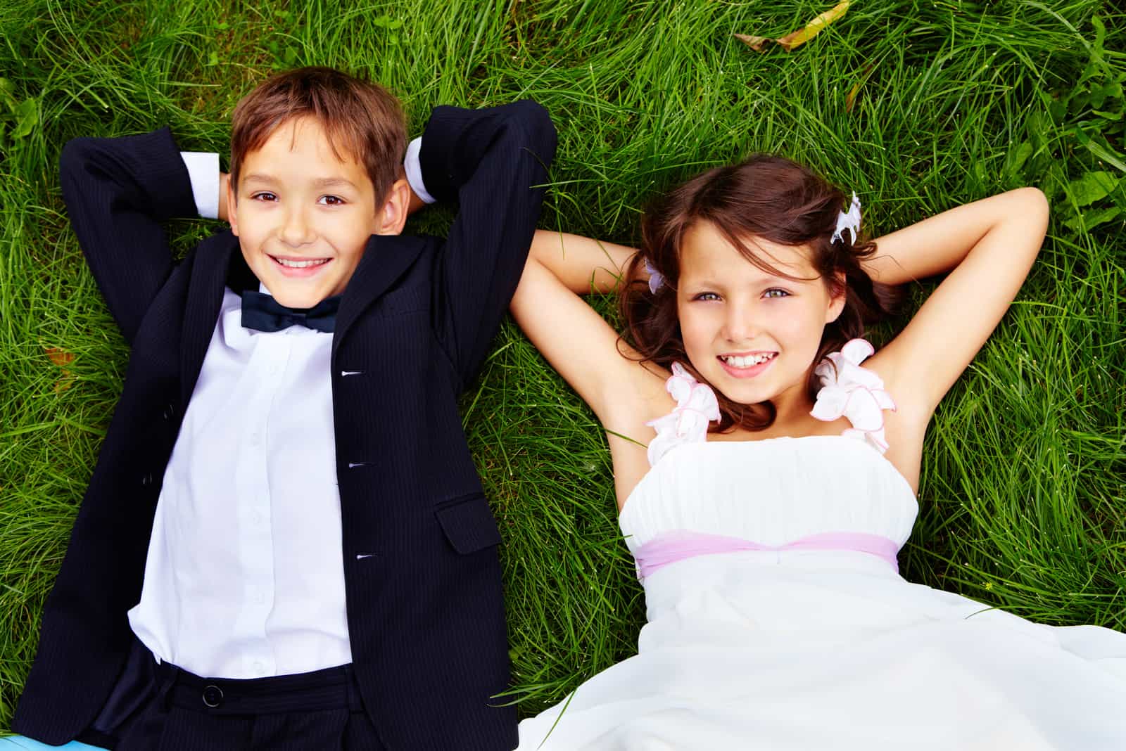 Porträt der Braut und des Bräutigams der lächelnden Kinder, die auf grünem Gras liegen und Kamera betrachten