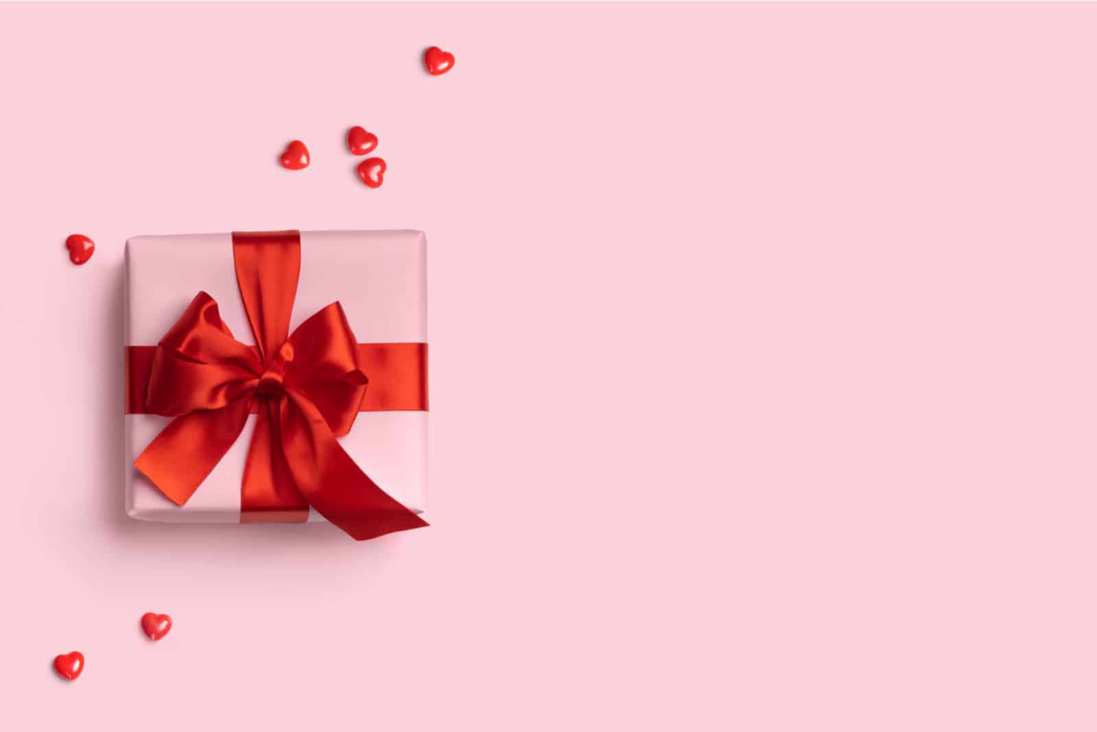 Rosa Geschenkbox mit roter Schleife auf rosa Hintergrund mit roten Herzen