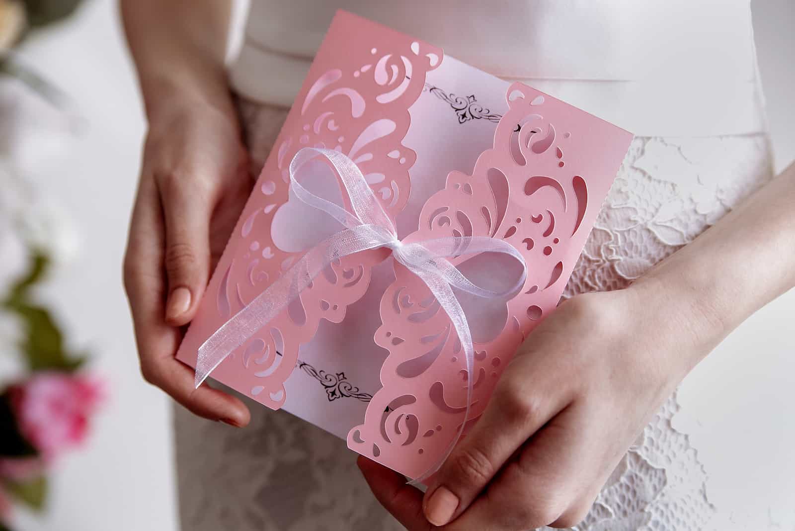 Rosa Karte der Hochzeitseinladung In den Händen der Braut