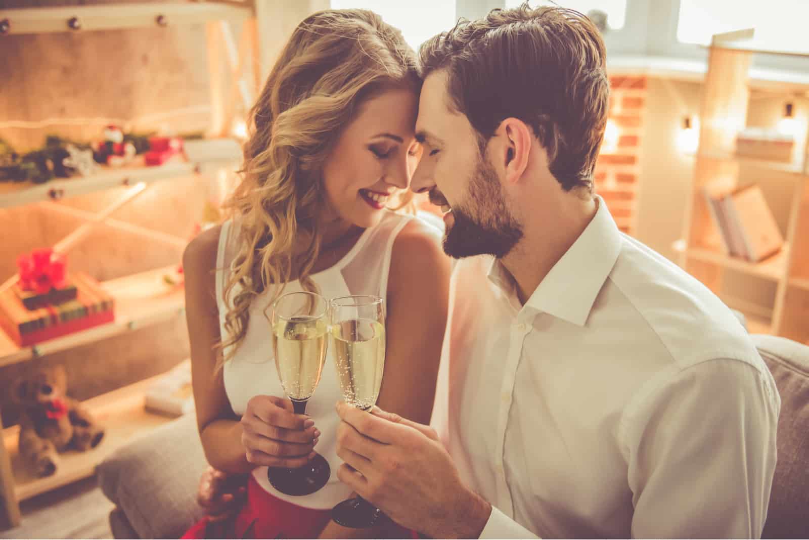 Schönes junges Paar hält Gläser Champagner und lächelt, während zu Hause feiern