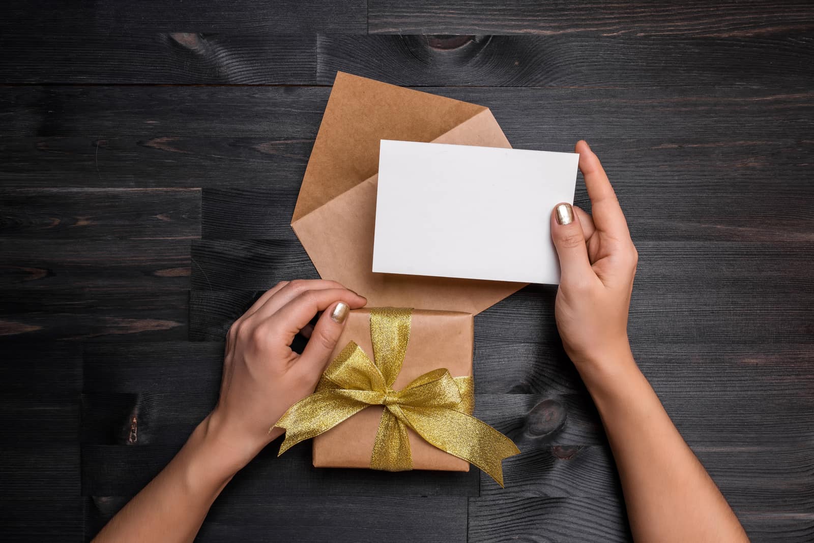 Weibliche Hände, die Geschenkkarte und Geschenkbox über dem schwarzen Holztisch halten