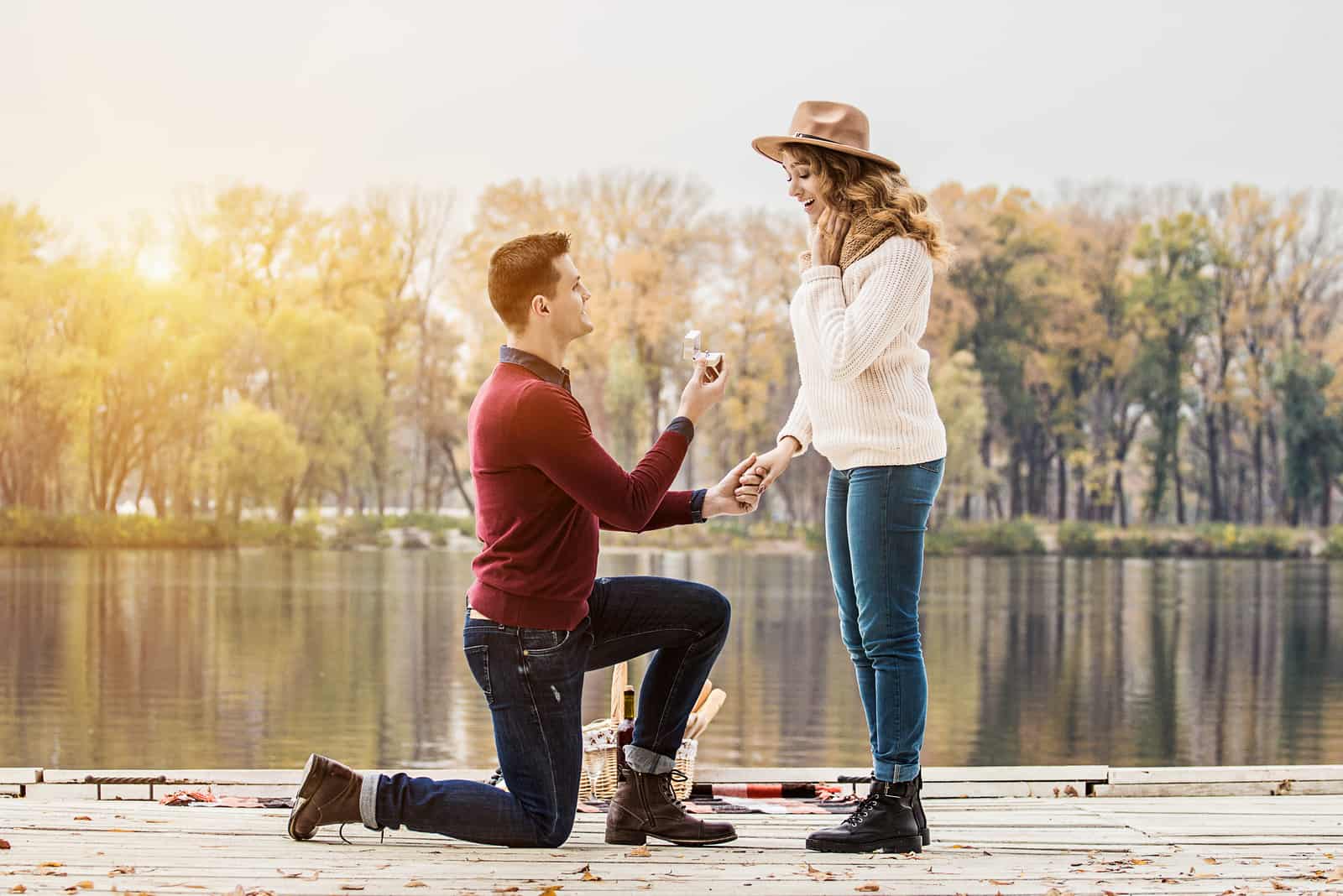 junger Mann in der Freizeitkleidung, die auf einem Knie steht und Verlobungsring hält, während Hochzeitsvorschlag macht