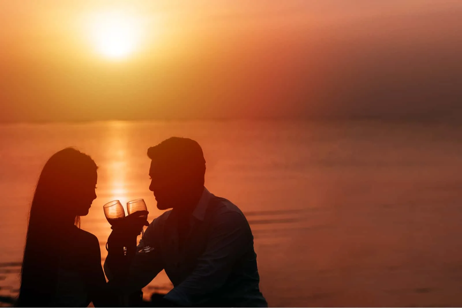 Am Strand bei Sonnenuntergang trinkt ein junges Paar Wein