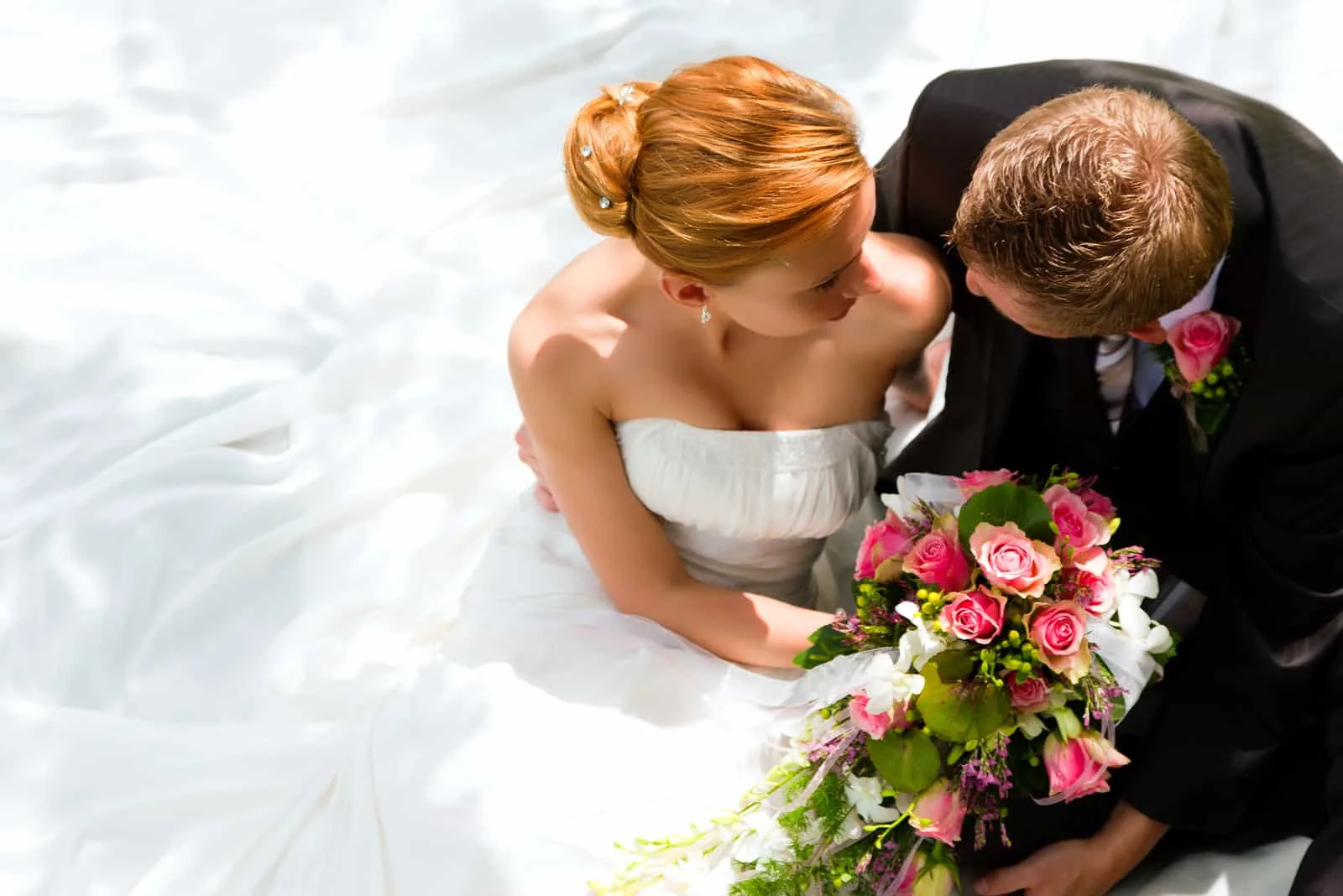Das Brautpaar sitzt mit einem Blumenstrauß und umarmt sich