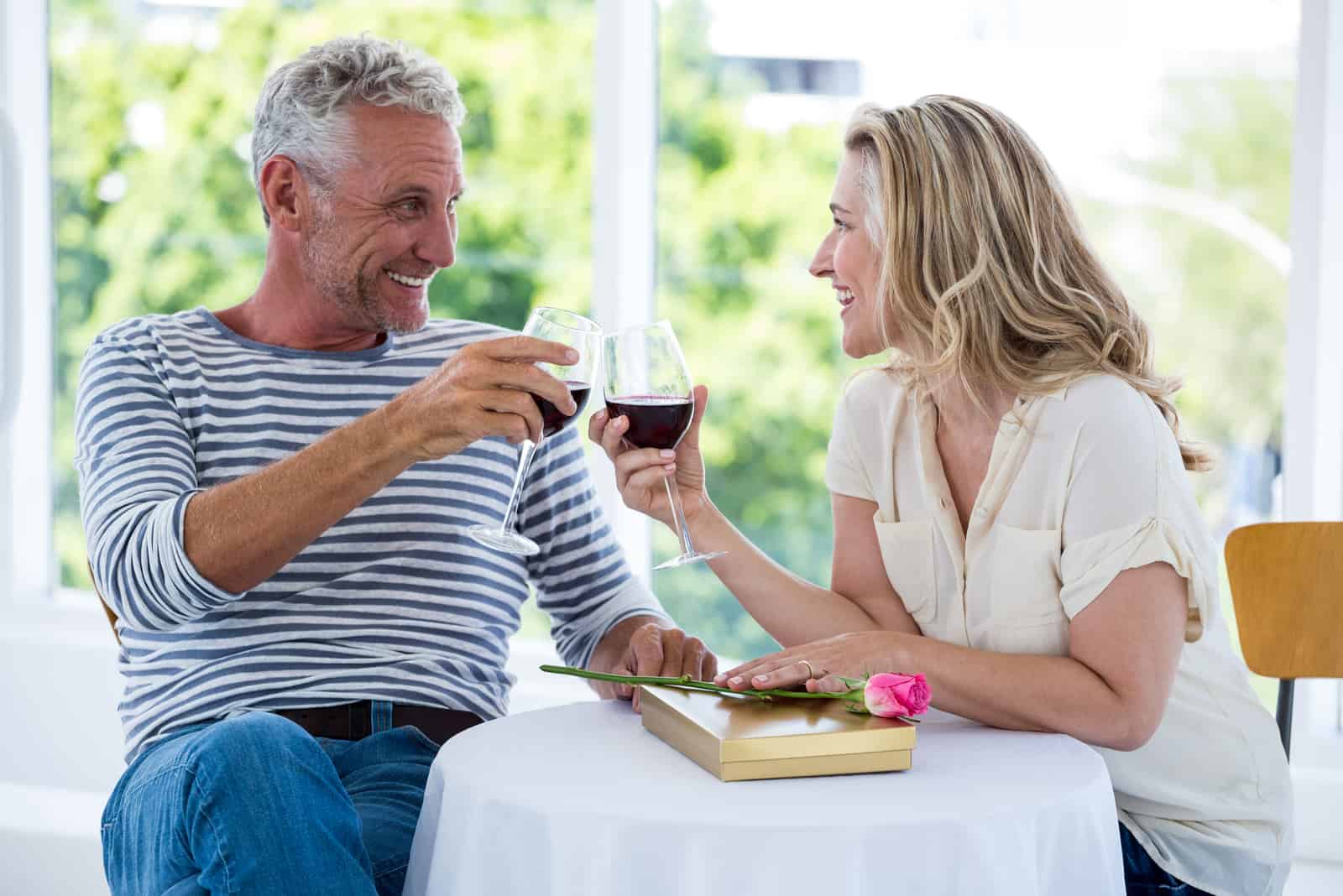 Das Paar sitzt auf der Terrasse und röstet mit Wein
