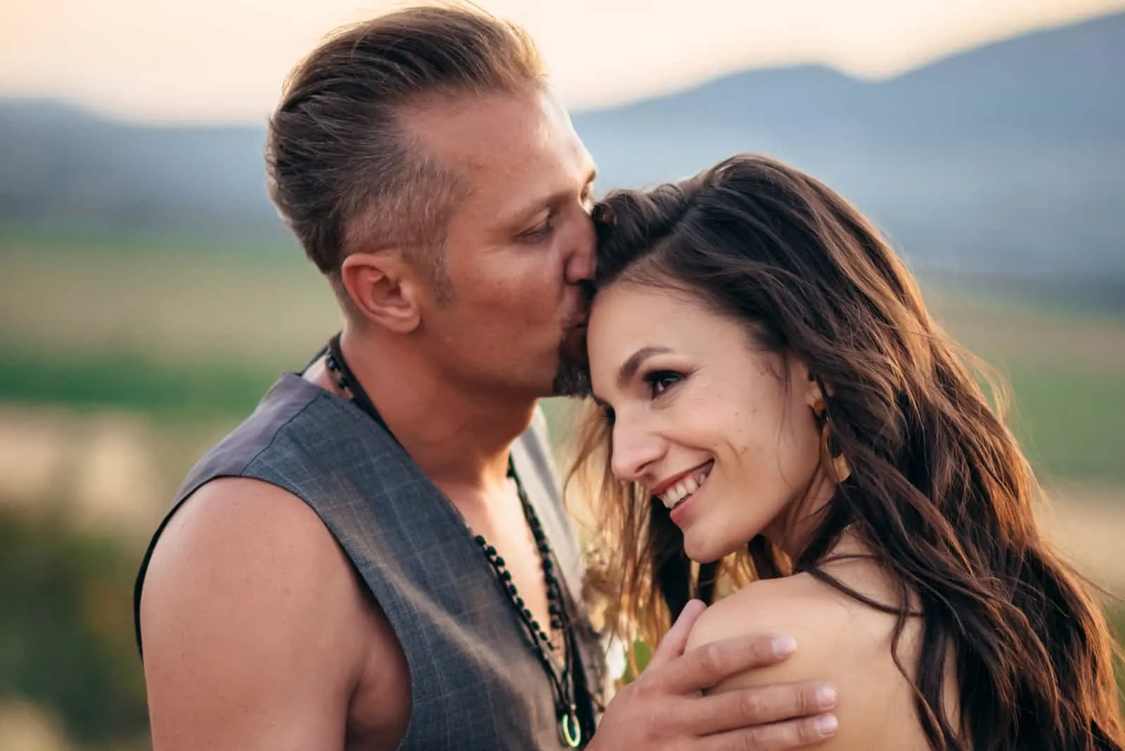 Ein Mann in einer Weste küsst eine lächelnde Frau auf die Stirn