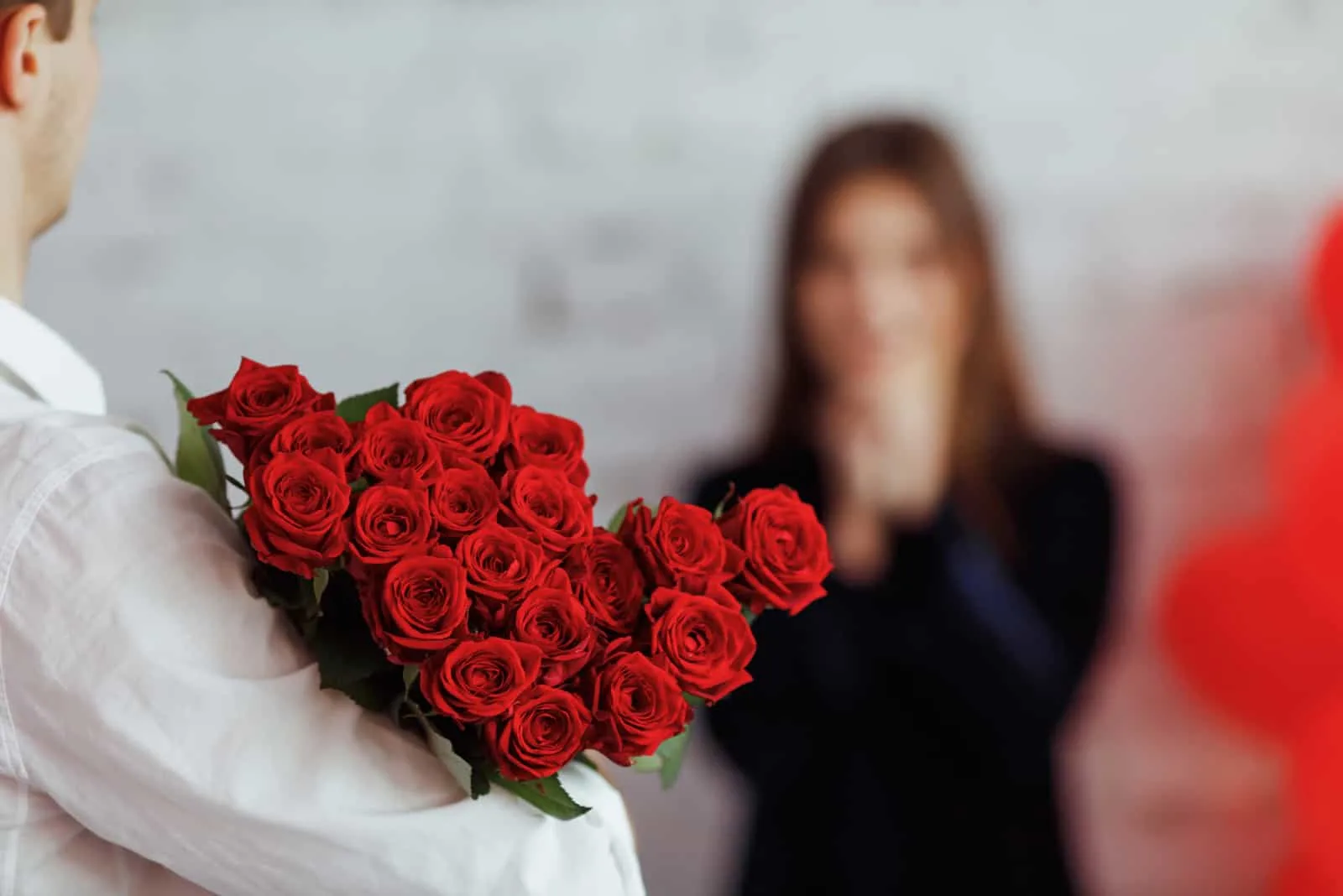Ein Mann präsentiert eine überraschte Frau mit einem großen Strauß roter Rosen