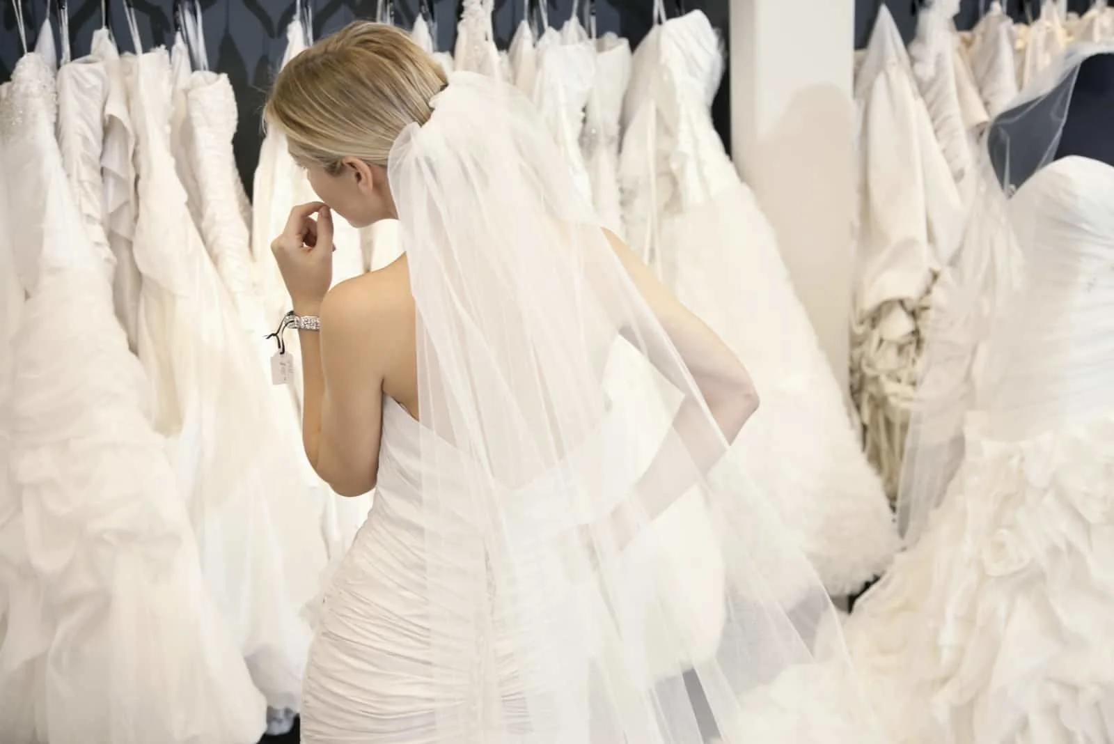 Hintere Ansicht einer jungen Frau im Hochzeitskleid, die Brautkleider auf Anzeige in der Boutique betrachtet