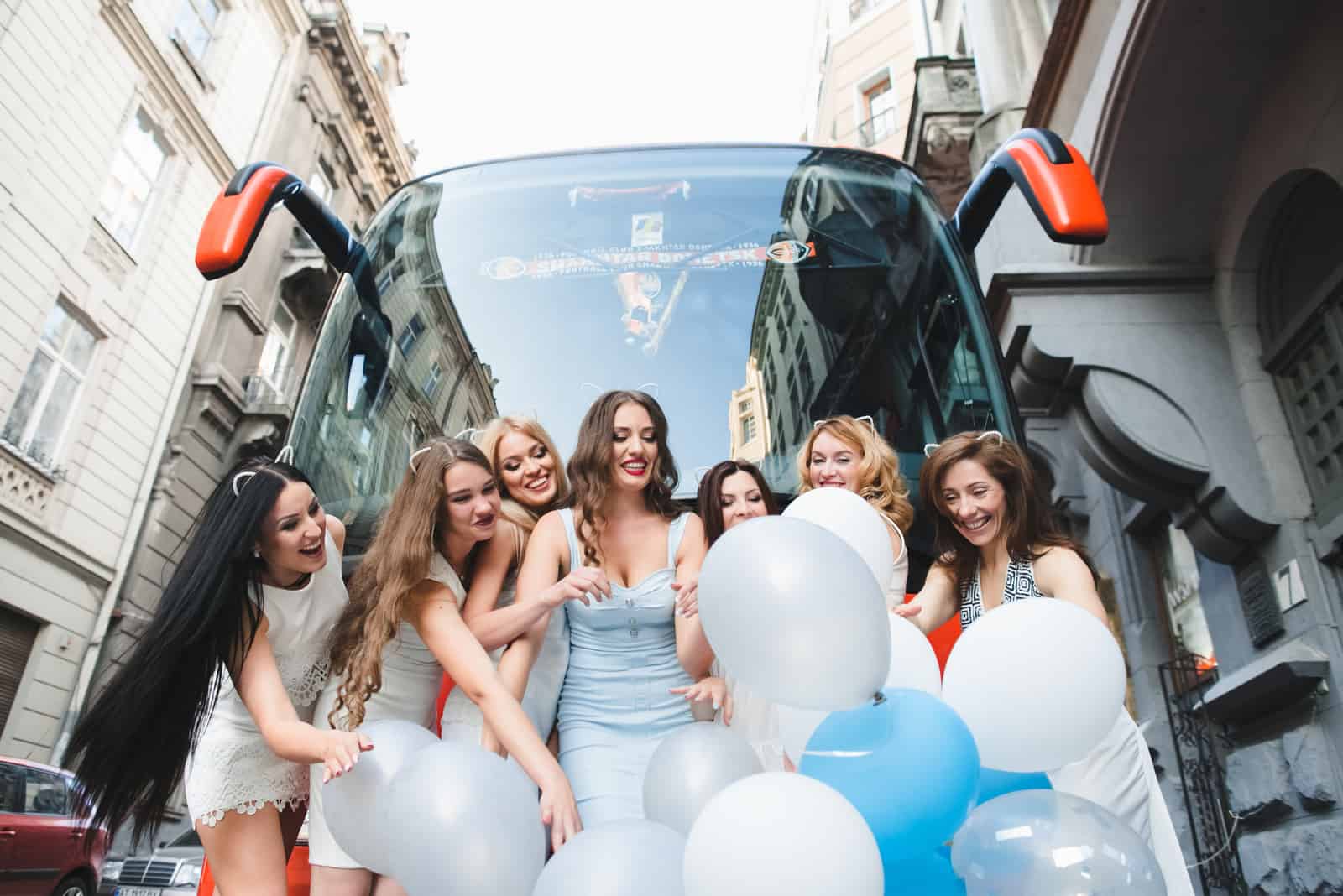 Vor dem Bus steht eine Gruppe lächelnder Mädchen mit Luftballons