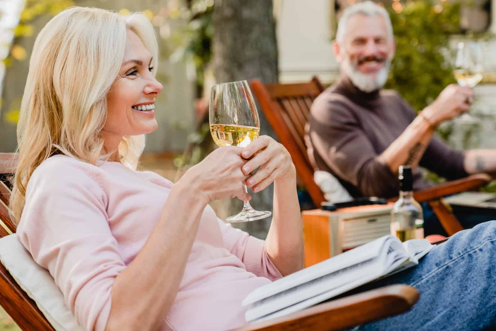 ein glückliches älteres Paar, das auf hölzernen Liegen sitzt und Wein trinkt