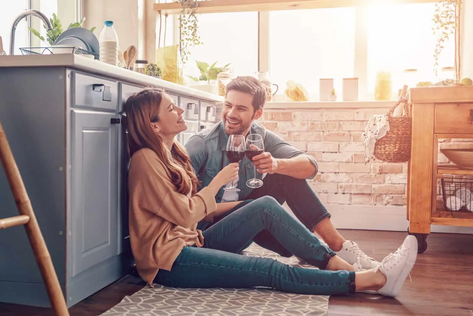 ein lächelndes Paar auf dem Küchenboden sitzt und trinkt Wein