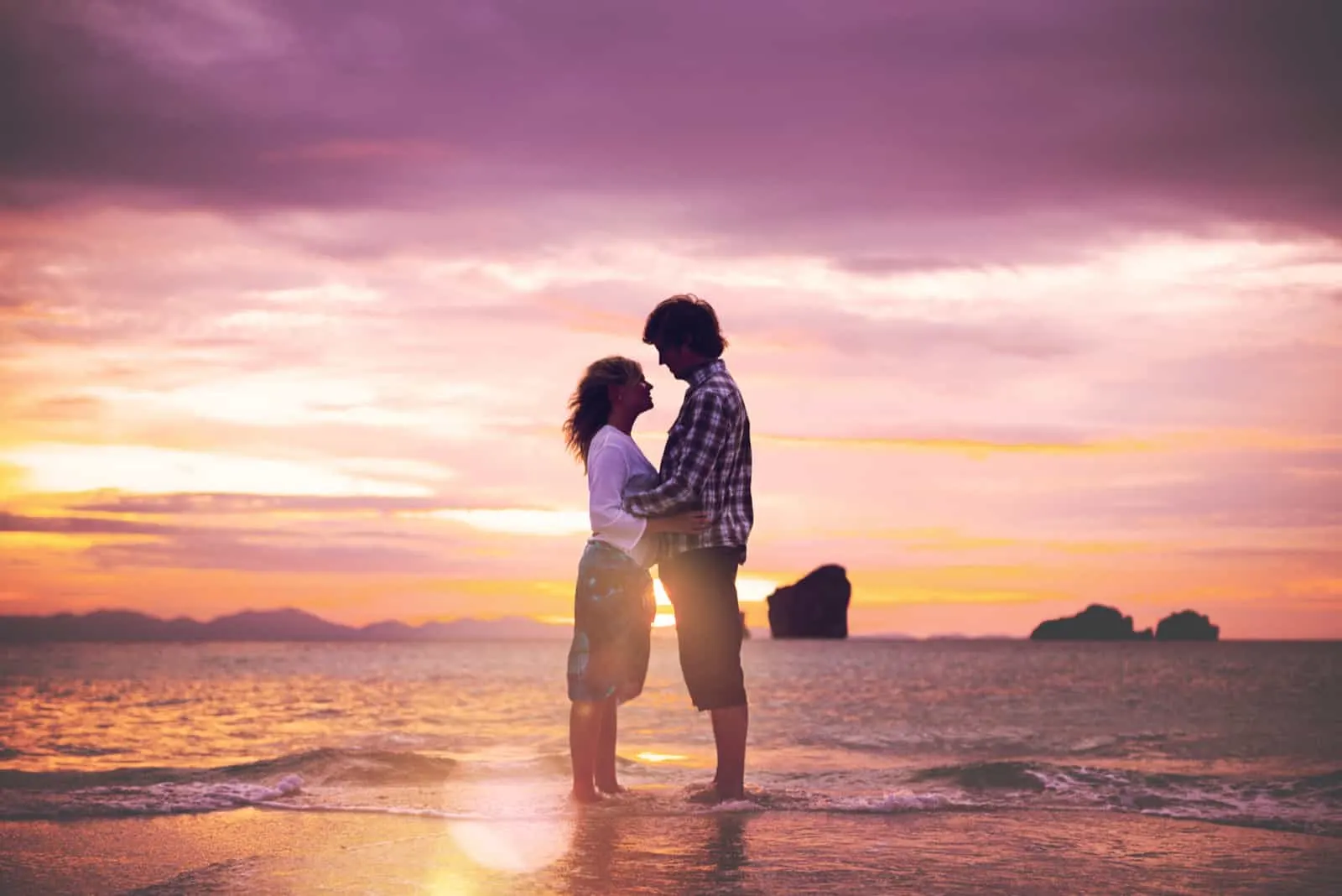 am Strand bei Sonnenuntergang ein liebevolles Paar umarmt und küsst