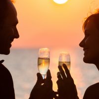 Paar bei Sonnenuntergang am Strand mit Gläsern Champagner