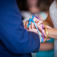Braut und Bräutigam Hände mit bunten blauen, lila und gelben Bändern gebunden