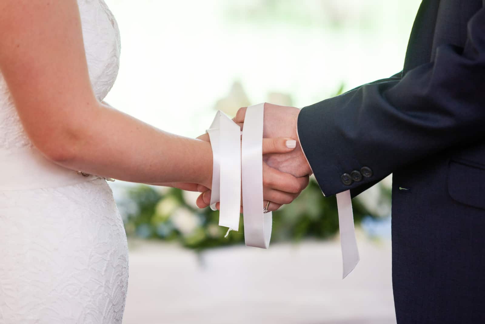 Moment der Hochzeitszeremonie, die Hände von Braut und Bräutigam mit weißen Bändern gebunden