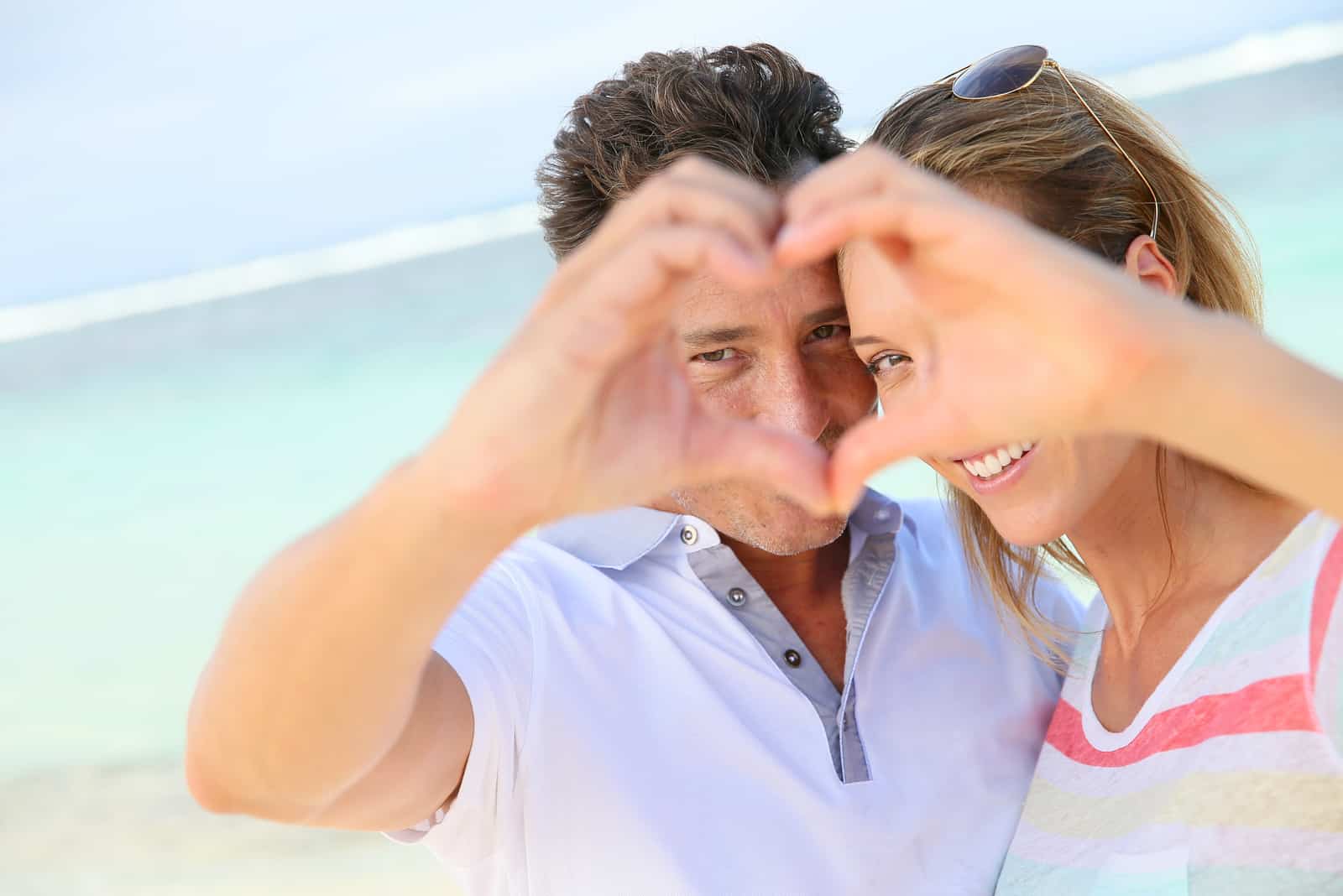 Romantisches Paar am Strand, das Herzzeichen mit den Händen macht