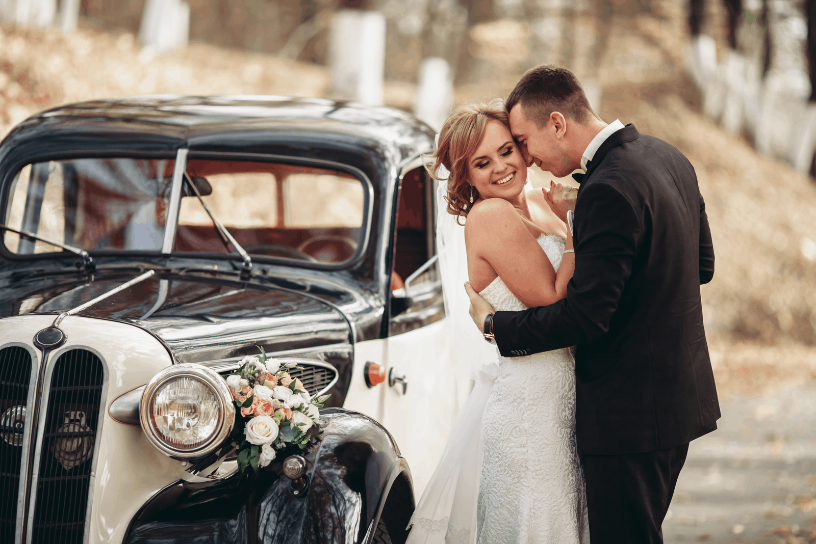 Hochzeitspaar küssen und umarmen sich in der Nähe von Retro mit Blumenstraußauto